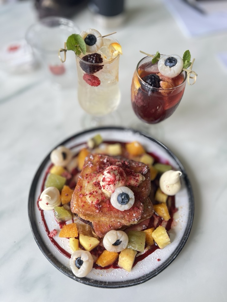 Brioche French toast with fruit and lychee-and-blueberry eyeballs, with two Halloween drinks behind
