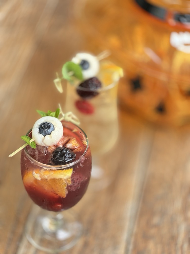 Deep red drink with orange slices and a lychee-and-blueberry eyeball garnish