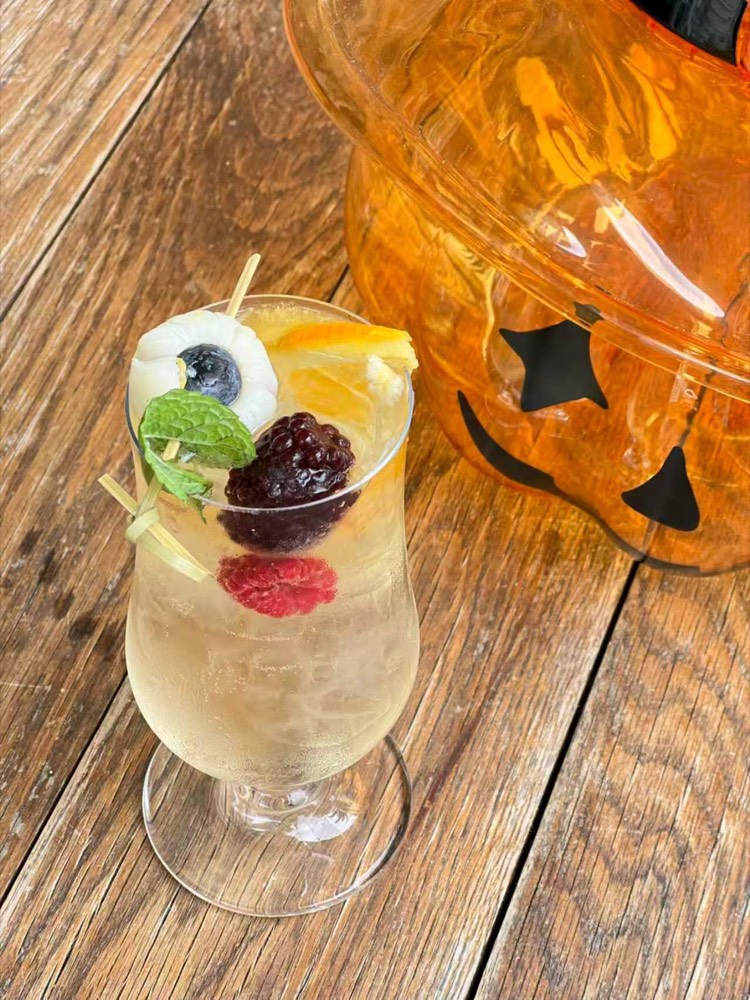 Pale sparkling drink with berries, mint and a lychee eyeball, beside a glass pumpkin jar
